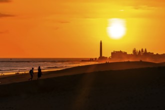 Tourists walking on the maspalomas dunes at sunset, with the maspalomas lighthouse in the