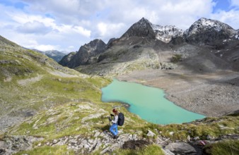 Hiker with rucksack looking at a turquoise-coloured mountain lake under a cloudy sky, Gradensee,