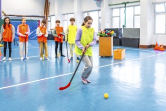 Group of elementary school students wearing vests practicing floorball in gym class, learning