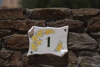 Yellow mimosas and the house number 1 can be seen on a ceramic sign, Bormes les Mimosas,
