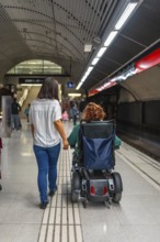 Rear view of a disabled woman and caregiver in the platform of the metro