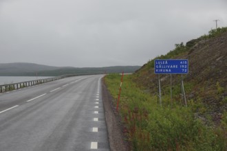Lonely country road under cloudy sky with road sign pointing towards Luleå and Kiruna, autumn in