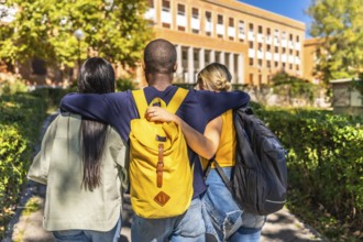 Rear view of three multi-ethnic students embracing while walking together to the university