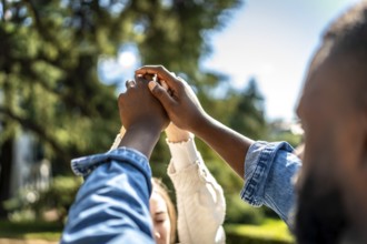 Multi-ethnic couple holding hands and raising them in a park