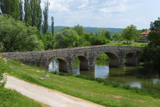 Stone bridge over a quiet river, surrounded by green nature under a blue sky, bridge over the river