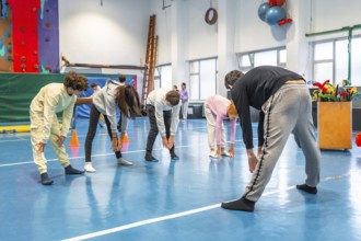 Teenagers bending forward and touching toes while exercising together in school gym class
