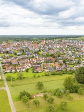 Aerial view of a village with red roofs, surrounded by green meadows and trees under a cloudy sky,