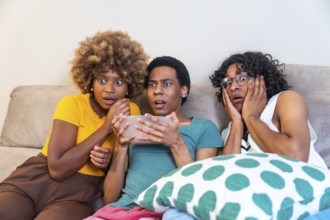 Multi-ethnic friends watching horror movie and eating pop corn sitting on the sofa at home