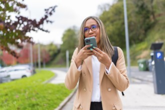Latin woman in casual business clothes sending voice message using phone walking along the city