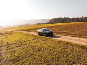 A black car on a dirt road in the middle of golden autumnal fields in sunlight, electric car VW