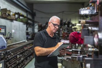 Concentrated mature male worker holding clipboard and writing while doing inventory in a