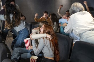 Enthusiastic friends are enjoying a movie at the cinema, hugging, cheering, and sharing a joyful