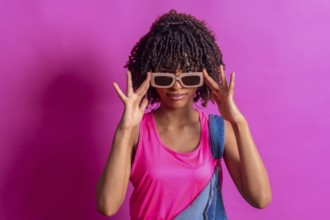 Fashionable young woman adjusting her sunglasses while posing against a vibrant pink backdrop