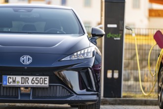 Front of a black electric car with licence plate next to a charging station, Deer E- Carsharing