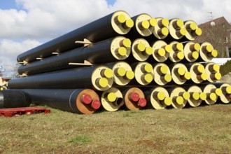 Stacked district heating pipes and district heating lines with yellow ends lie piled up in a meadow