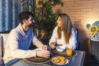 Smiling couple having breakfast together on their balcony, enjoying a peaceful moment with orange