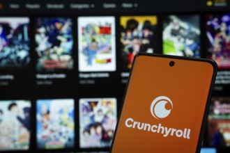 Crunchyroll logo is displayed on a smartphone screen, with the crunchyroll website visible on a