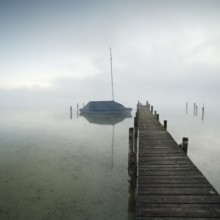 Quiet autumn morning on Lake Chiemsee, jetty with sailing boat in dense fog, Prien am Chiemsee,