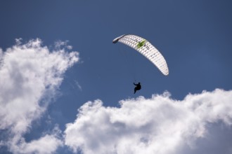 A person floats with a paraglider high in the sky in front of white clouds