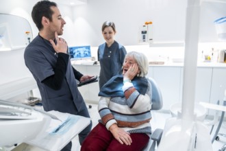 Senior woman suffering from toothache discussing treatment options with dentist and nurse in a