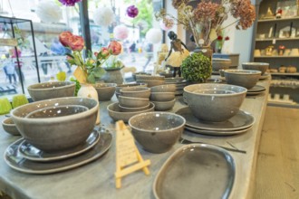 Tableware set in shades of grey on a table surrounded by floral decorations in front of a window,