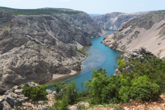 The river meanders through a stony gorge with turquoise blue water, surrounded by green trees,