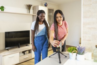 Two teenage girls preparing equipment for recording video content at home, using smartphone and