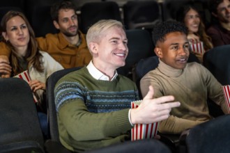 Group of diverse friends watching a film at the movie theater, commenting the scene and smiling,