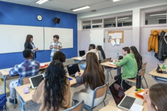 Multi ethnic group of high school students attending a lesson with two teachers and using laptops