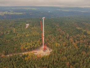 A tall crane erects a wind turbine in the dense autumn forest, wind farm construction site,