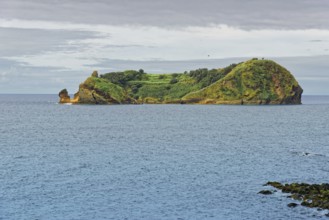 Green, rocky island and protected area Ilhéu de Vila Franca do Campoin a calm sea under a cloudy