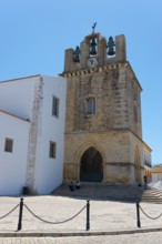 Historic church with bell tower, surrounded by white buildings, under a bright blue sky, Sé