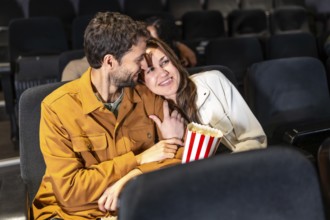 Romantic couple enjoying a movie night, sharing popcorn and affection in a comfortable cinema seat