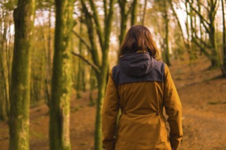 Lifestyle, a young woman in a yellow jacket walking backwards along a forest path in autumn.