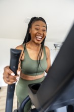 Cheerful black woman enjoys her workout on an elliptical trainer, maintaining her fitness routine