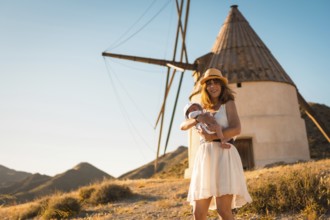 Mother holding a newborn baby next to a windmill in Cabo de Gata, Spain