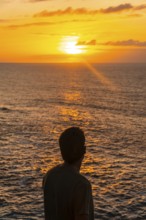 Silhouette of tourist contemplating beautiful golden sunset over atlantic ocean in agaete, gran