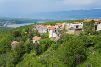 View of a village with red roofs, embedded in green vegetation and with mountains in the