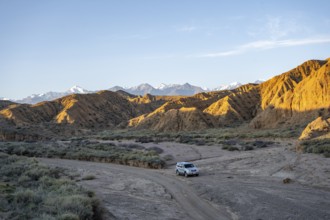 Off-road vehicle driving through a canyon, landscape of eroded hills at sunrise, badlands, white