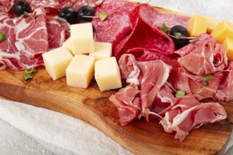 Assorted, sliced meat appetizer, prosciutto, salami and ham, with cheese and olives, on a wooden