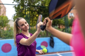 Smiling sportive blonde woman shaking racket with partner in a pickelball court