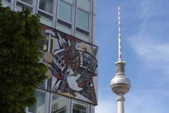 Television tower and building with wall mosaic and tree in front of blue sky, combination of art