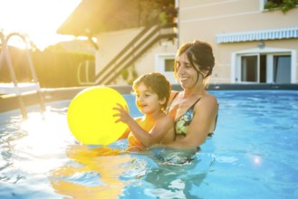 Mother and son having fun together in a home swimming pool, playing with a yellow inflatable ball