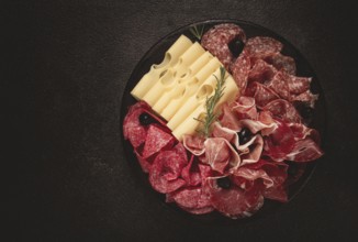 Cold cuts, appetizer, prosciutto, salami and ham, with maasdam cheese and olives, on a round plate,