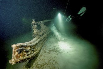 Underwater image of a diver approaching a shipwreck with a light source, dive site wreck of the