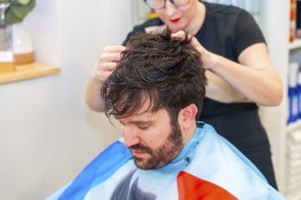 Hairstylist attaching a new capillary prosthesis to a man's head sitting on a salon