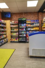 A supermarket interior with modern shelving and refrigeration units in front of a brick wall, Tante