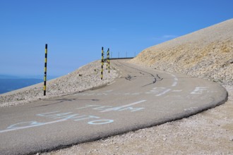 Winding road on a barren hill under a clear blue sky with yellow posts at the edge, Mont Ventoux,