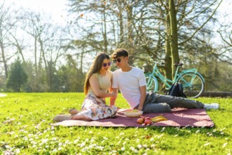 Happy couple sharing a romantic picnic in a sunny park with their bicycle nearby, enjoying fresh