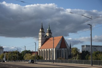 Close-up of St John's Church with two towers and red roof, next to a street and under a sky with